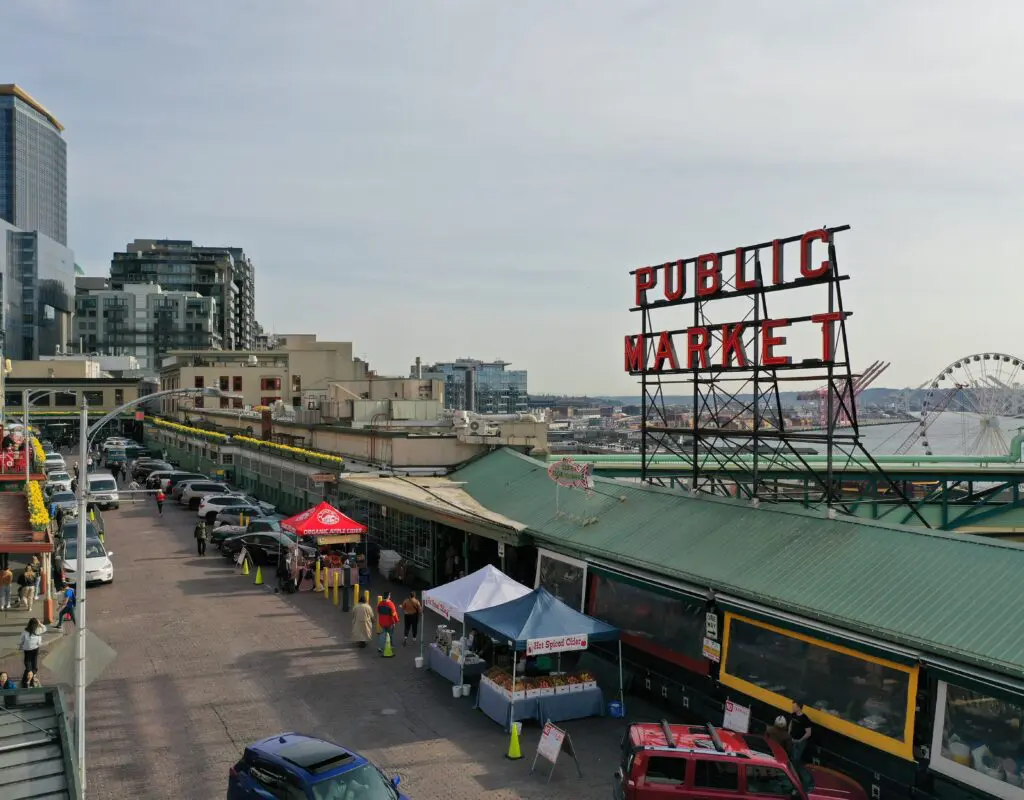 Iconic Public Market sign at Pike Place Market, Seattle. The colorful market is in the foreground while the vibrant sign surround by downtown condos and the Great Wheel captures the essence of this bustling landmark, inviting visitors to explore a world of fresh produce, artisanal goods, and rich cultural heritage